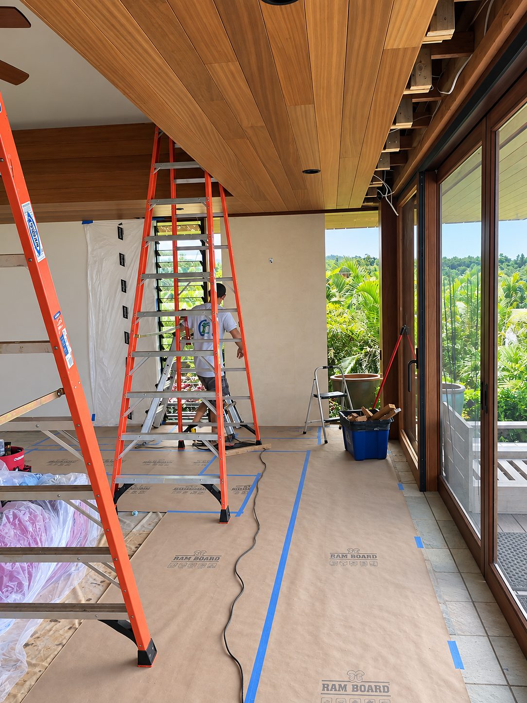Floors protected with paper, ladders up and blue tape lines under the ceiling framing of an occupied home